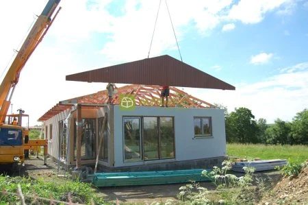 Výstavba prefabrikovaného domu s montáží střechy pomocí kranu.