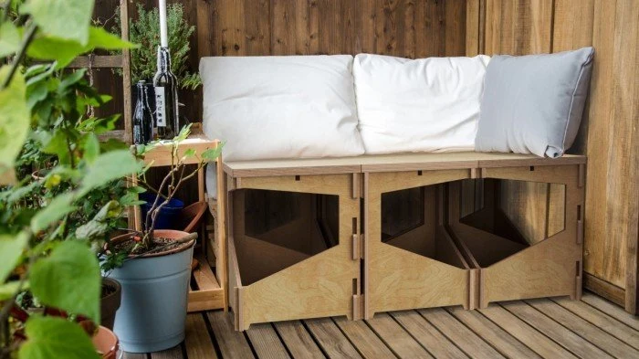 Dřevěná lavička s polštáři na balkóně obklopená rostlinami.