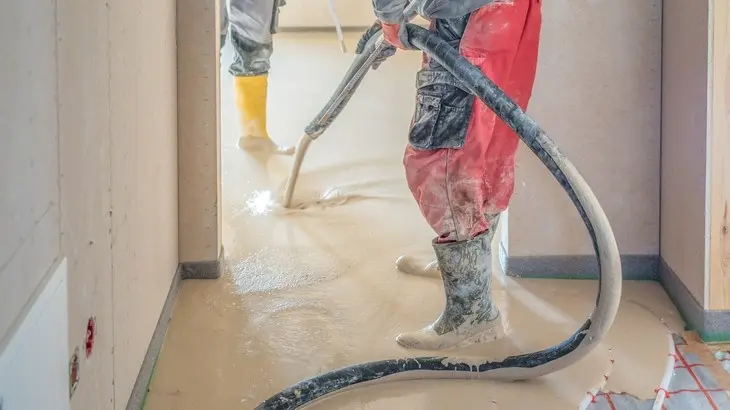 Práce s anhydrytem: aplikace tekuté směsi na podlahu pomocí hadice.