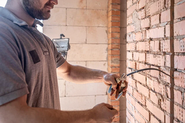 Muž řezá kabel na zdi během instalace.