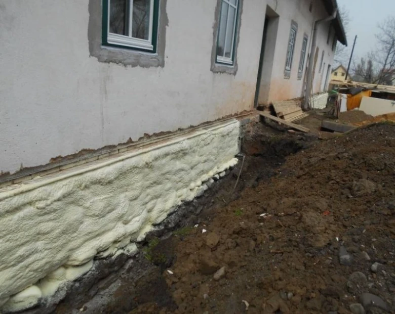 Nanášení izolační pěny na zdivo soklu domu.