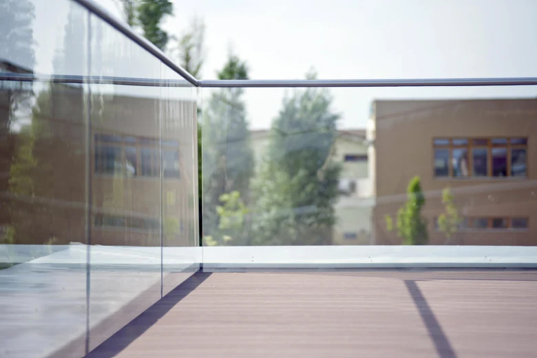 Moderní skleněné zábradlí na dřevěném balkónu s odrazy okolních staveb.