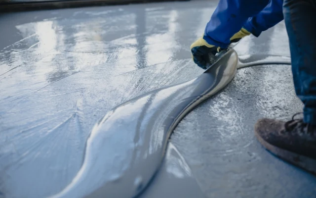 Práce s samonivelačním betonem při stírání podlahy.