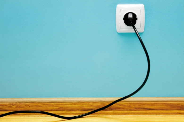 Černá elektrická zástrčka v zásuvce na modré stěně.
