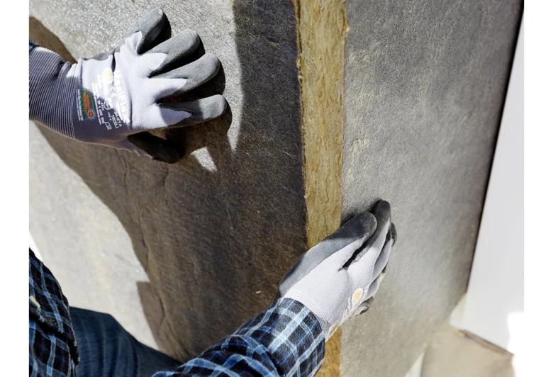 Ruce v rukavicích přitiskují desku zateplovacího materiálu na roh fasády.