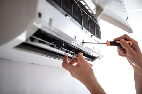 Ruční oprava klimatizace šroubovákem uvnitř jednotky.