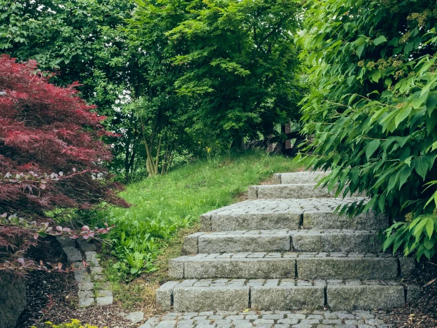 Kamenné schody vedoucí po svahu v zeleném zahradním prostředí.