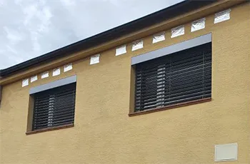Žaluzie a rolety na střešní okna v žluté fasádě.