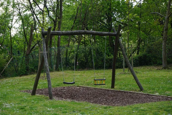 Dřevěná houpačka na zahradě s dvěma sedacími křesly.