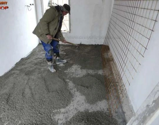 Stavebník rozlévá anhydritovou směs na podlahu.