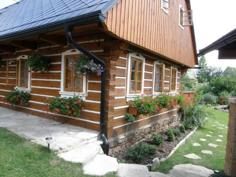 Tradiční roubená chalupa s květinovými boxy na oknech.