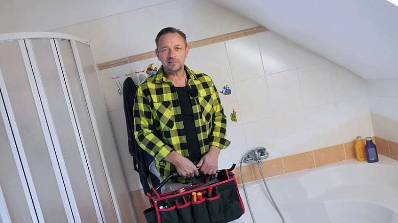Muž s nářadím pro opravu sprchy a baterie v koupelně.