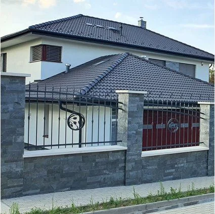 Moderní venkovní fasáda s kamenitým obkladem a kovovým plotem.
