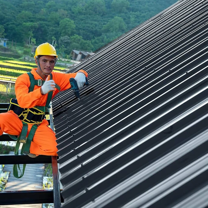 Montáž trapézových plechů na střechu pracovníkem s elektrickým vrtákem.
