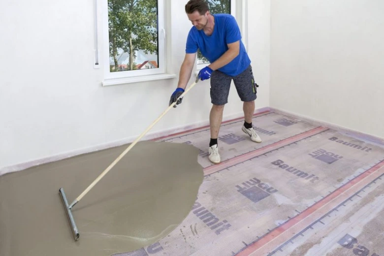 Muž nanáší hydroizolační nátěr na podlahu v interiéru.