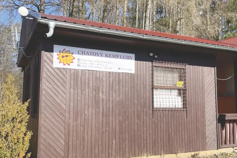 Exteriér chaty v kempu Milavy s výrazným nápisem na fasádě.