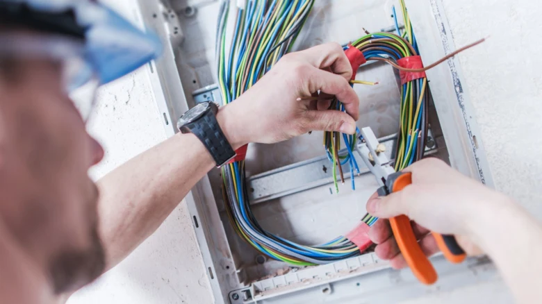Elektrikář pracuje s kabely v rozvaděči při instalaci.
