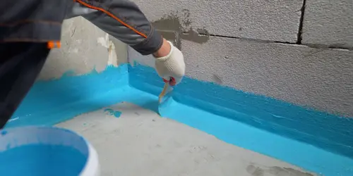 Práce na hydroizolaci podlahy v koupelně pomocí modré barvy.