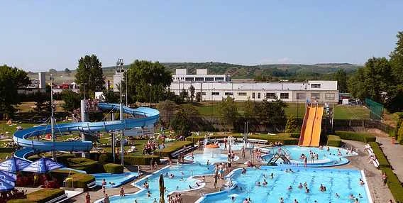 Venkovní aquapark s vodními skluzavkami a bazény plnými lidí.
