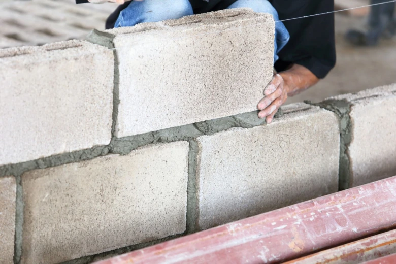 Stavebník kladí betonové cihly do zdiva s maltou.