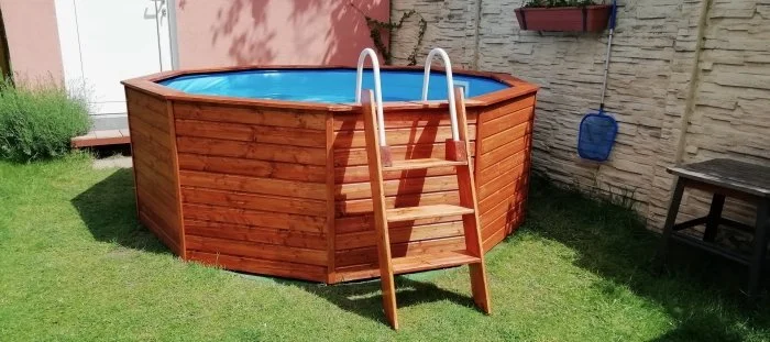 Nadzemní bazén s dřevěným obložením na trávníku.