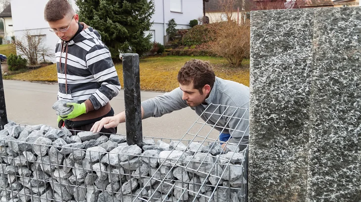 Muži plní drátěný koš kameny pro stavbu gabiónu.