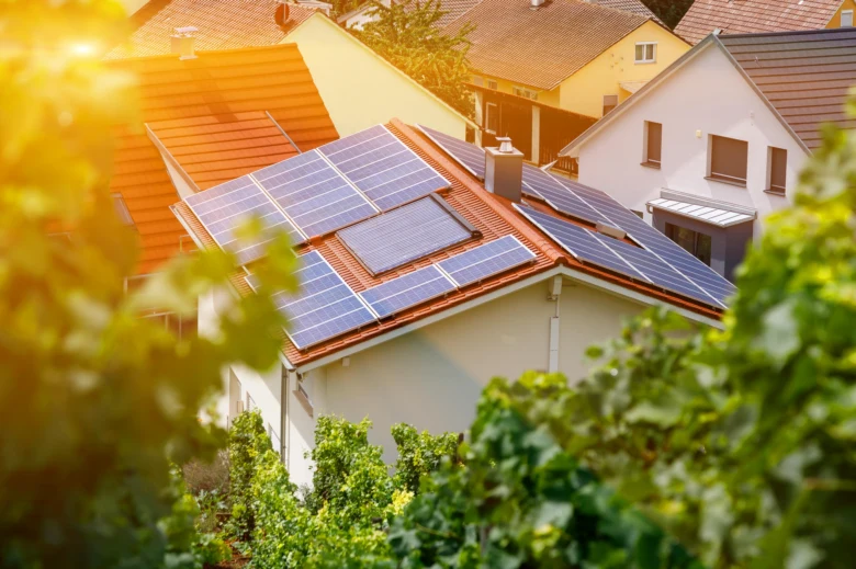 Fotovoltaické panely na střeše rodinného domu v zeleném okolí.