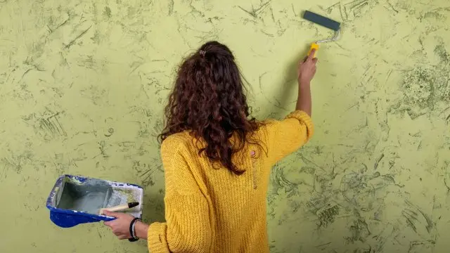 Žena aplikuje texturovaný vzor na zeď pomocí válečku.