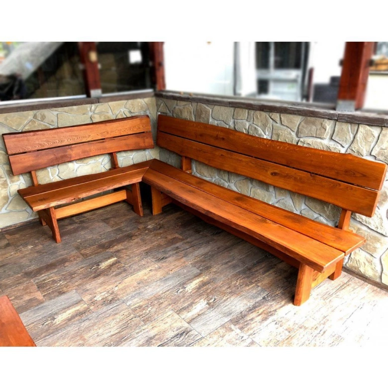 Dvě dřevěné rohové lavice na balkoně u kamenné zdi.