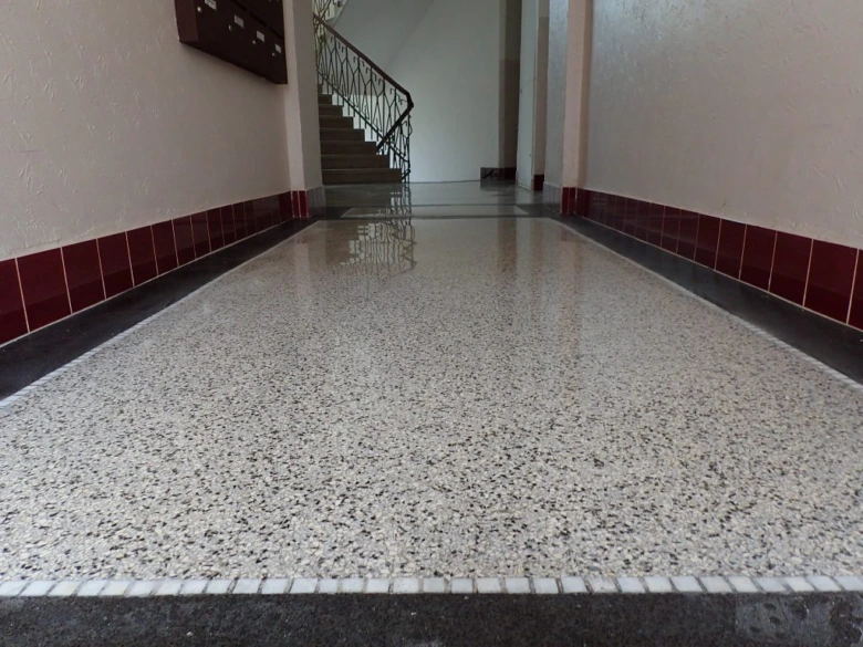 Lesklá dlažba z terazzo v chodbě vedoucí ke schodům.