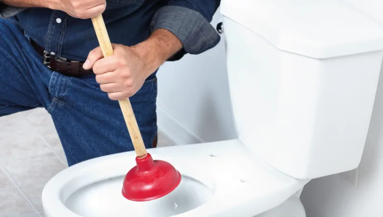 Muž používá hadicovou pumpu na záchod pro uvolnění ucpaní.
