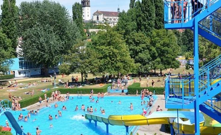 Venkovní plavecký bazén s kluzáky a lidmi koupející se v Praze.