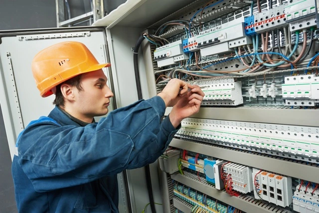 Elektrikář pracuje na průmyslovém elektrickém rozvaděči s kabely.