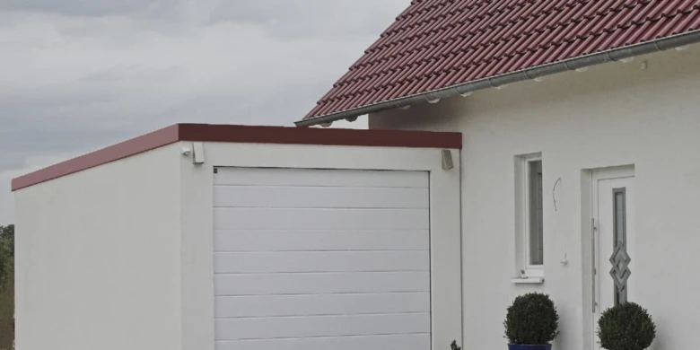 Bílá samostatná garáž připojená k domu s červenou střechou.