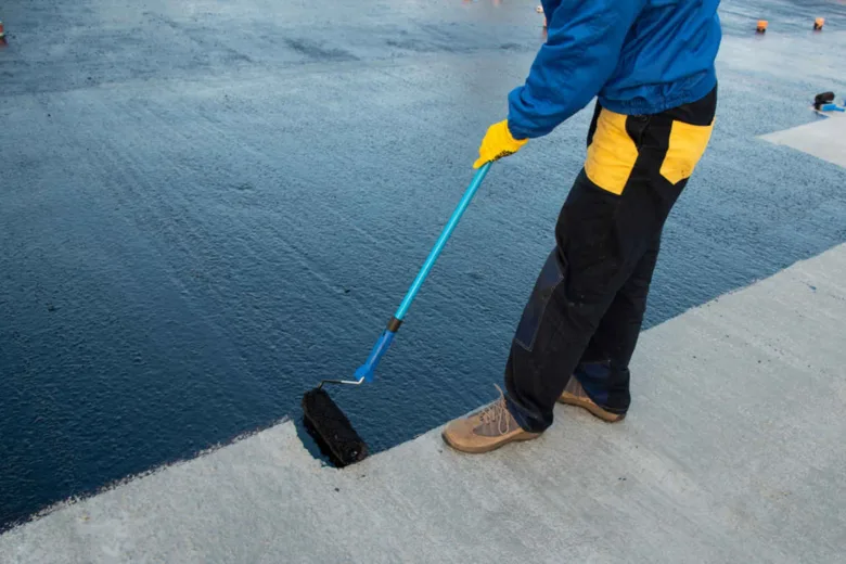 Pracovník nanáší tekutou hydroizolaci válcem na betonovou plochu.