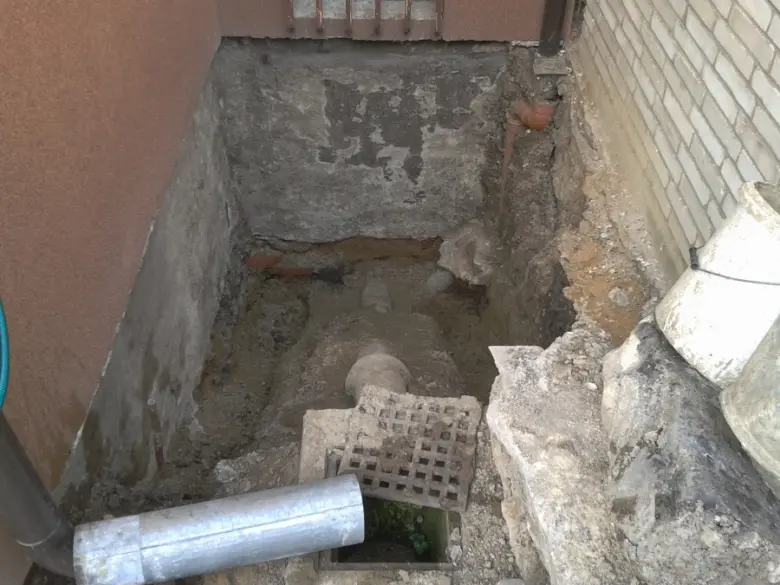 Vykopaná příkopová jáma u vstupu do sklepa s viditelnými potrubími.