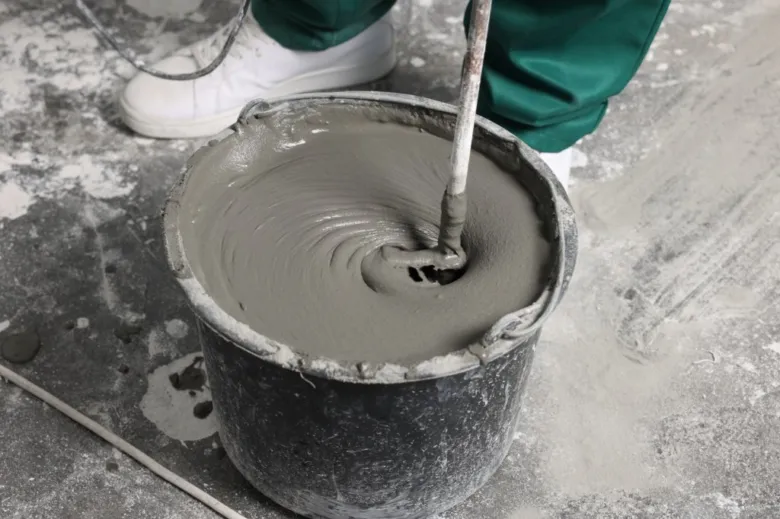 Pracovník míchá beton v kbelíku na staveništi.