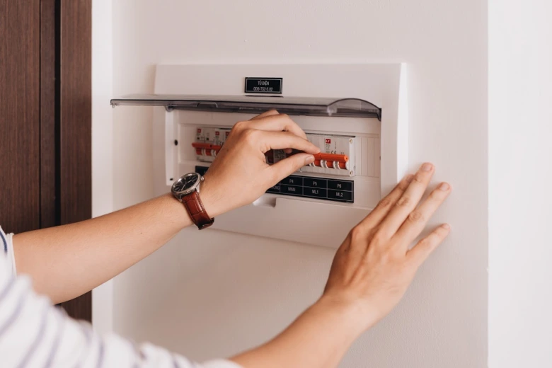 Ruka otvírá jistič v elektrickém rozvaděči na zdi.