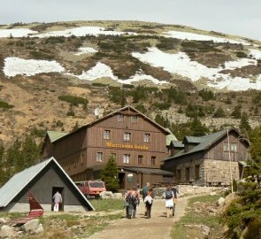 Skupina turistů kráčí k horské chatě Martina Boudy na sněžné hoře.