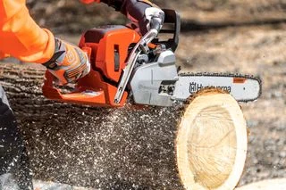 Člověk řezí dřevo motorovou pilou značky Husqvarna.