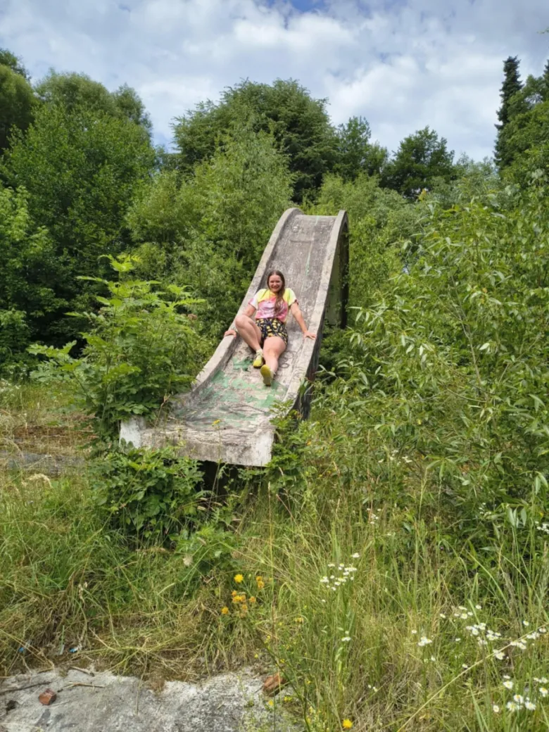 Žena sedí na opuštěném betonovém skluzavce v zarostlé přírodě.
