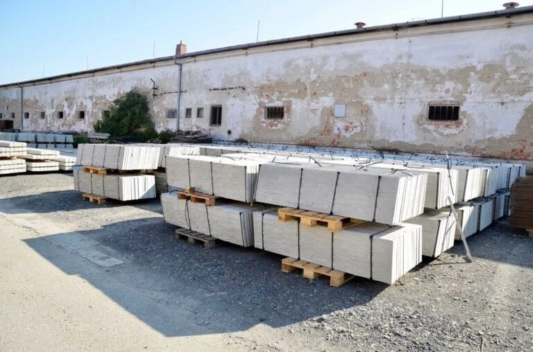 Nakládané betonové panely na paletách před starou budovou.