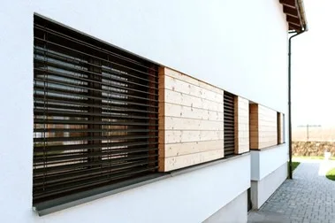 Venkovní žaluzie na bílém domě s dřevěnými panely.