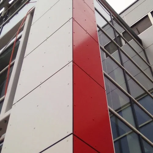 Bílé a červené fasádní desky na budově s okny.