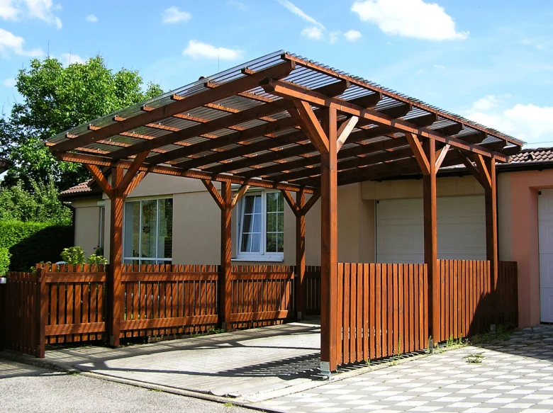 Dřevěný přístřešek pro auto u domu s plátovanou střechou.
