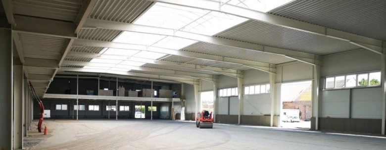 Vnitřek budovy skladové haly s ocelovými nosníky a betonovou podlahou.