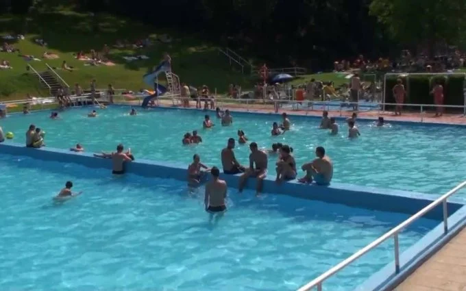 Lidé plavou v bazénu na koupališti v přírodě.