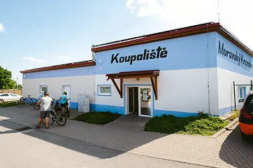 Vnější pohled na koupaliště v Moravském Krumlově s lidmi u vstupu.