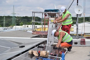 Dva dělníci montují fotovoltaické panely na střeše.