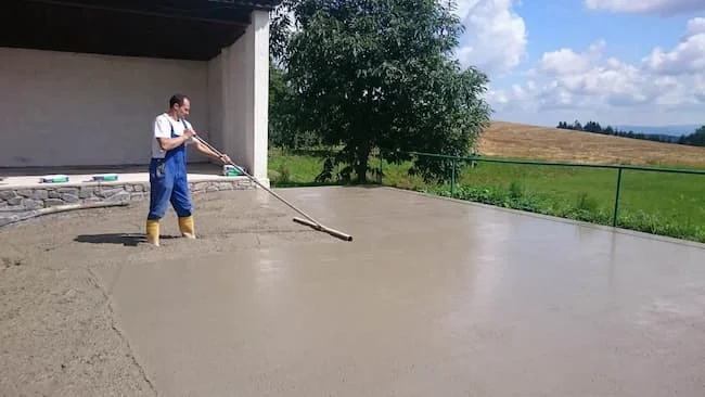Muž nalévá čerstvý beton na podlahu garáže nebo terasy.